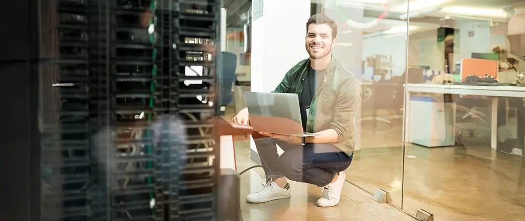 Person working on laptop near server racks in a modern office environment